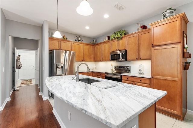 kitchen featuring sink, an island with sink, decorative light fixtures, appliances with stainless steel finishes, and light wood-type flooring