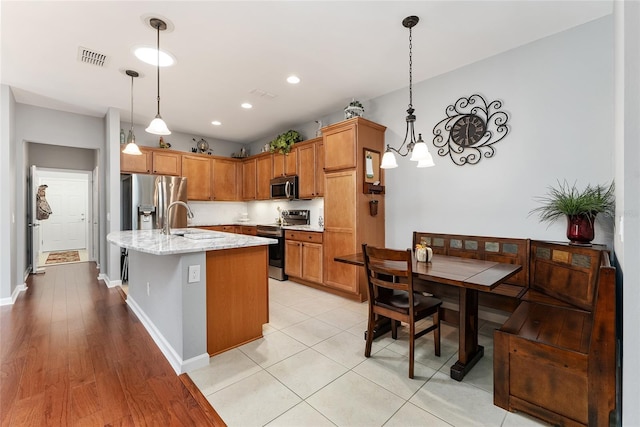 kitchen with light stone countertops, stainless steel appliances, pendant lighting, a center island with sink, and light hardwood / wood-style flooring