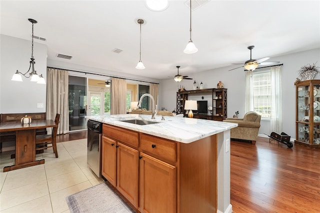 kitchen with a center island with sink, sink, hanging light fixtures, light hardwood / wood-style floors, and light stone counters