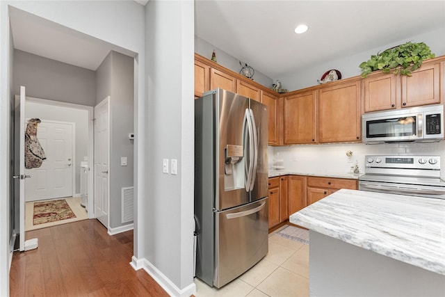 kitchen with backsplash, light stone countertops, stainless steel appliances, and light wood-type flooring