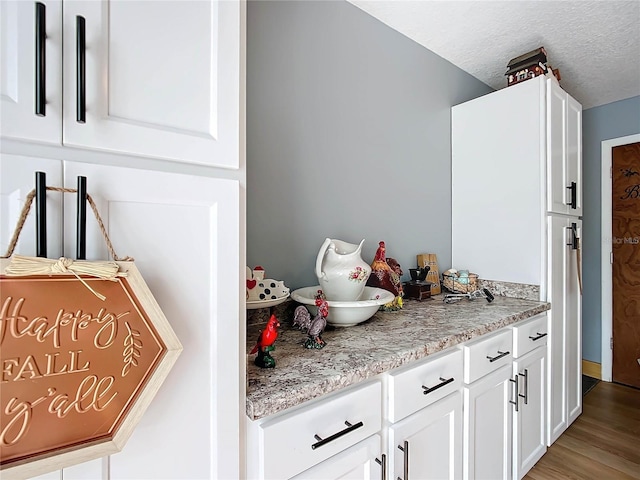 kitchen featuring white cabinetry, light stone counters, a textured ceiling, and light wood-type flooring