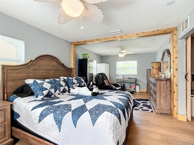 bedroom with stainless steel fridge, beam ceiling, light hardwood / wood-style floors, and ceiling fan