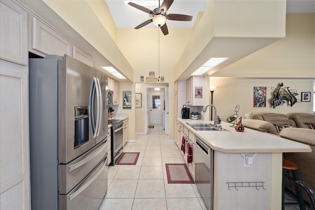 kitchen with light tile patterned flooring, a sink, light countertops, appliances with stainless steel finishes, and a kitchen bar