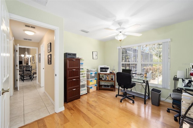 home office featuring light wood-type flooring, visible vents, and ceiling fan with notable chandelier