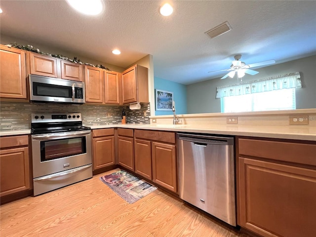 kitchen with backsplash, light hardwood / wood-style flooring, ceiling fan, a textured ceiling, and stainless steel appliances