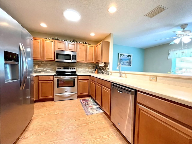 kitchen featuring backsplash, a textured ceiling, stainless steel appliances, sink, and light hardwood / wood-style floors