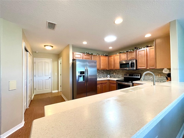 kitchen featuring sink, dark hardwood / wood-style floors, backsplash, kitchen peninsula, and appliances with stainless steel finishes