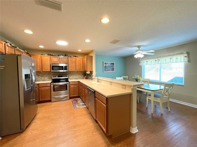 kitchen with light wood-type flooring, kitchen peninsula, sink, and appliances with stainless steel finishes