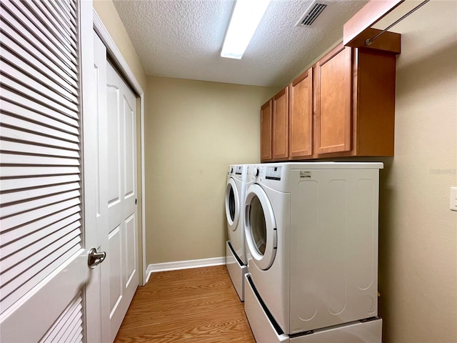 clothes washing area with light hardwood / wood-style floors, cabinets, separate washer and dryer, and a textured ceiling