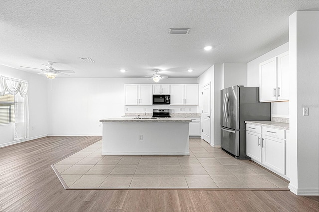 kitchen with appliances with stainless steel finishes, light wood-type flooring, sink, white cabinetry, and an island with sink