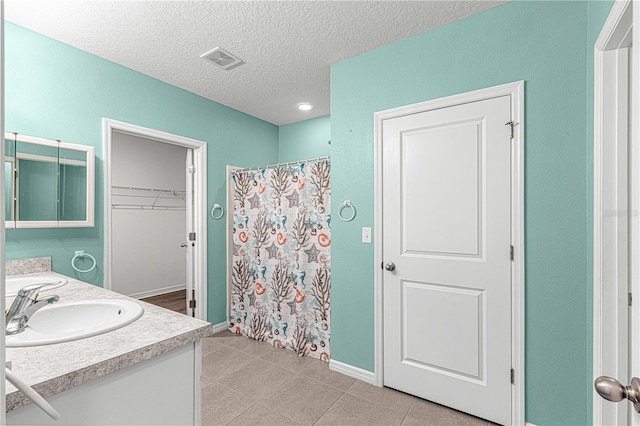 bathroom with tile patterned floors, vanity, a textured ceiling, and walk in shower