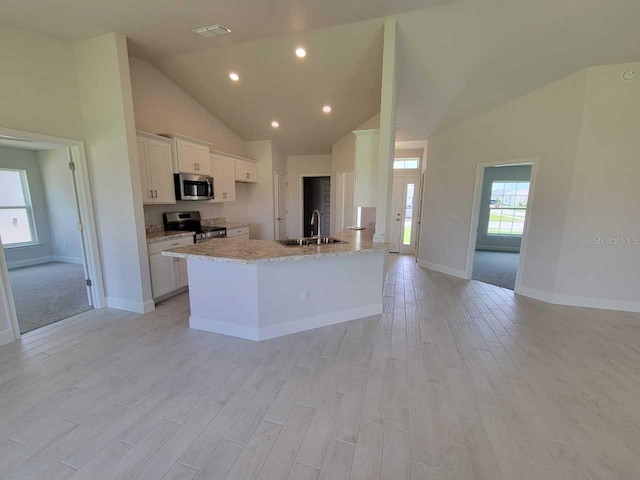 kitchen with high vaulted ceiling, stainless steel appliances, white cabinetry, and a wealth of natural light