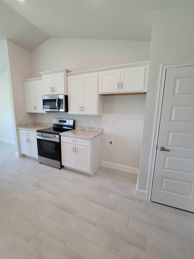 kitchen featuring white cabinetry, light stone countertops, lofted ceiling, and appliances with stainless steel finishes