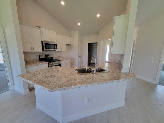 kitchen with appliances with stainless steel finishes, a sink, vaulted ceiling, a peninsula, and white cabinets