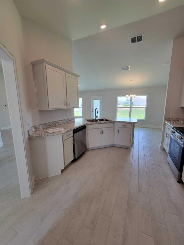 kitchen featuring light wood finished floors, a peninsula, a sink, baseboards, and appliances with stainless steel finishes