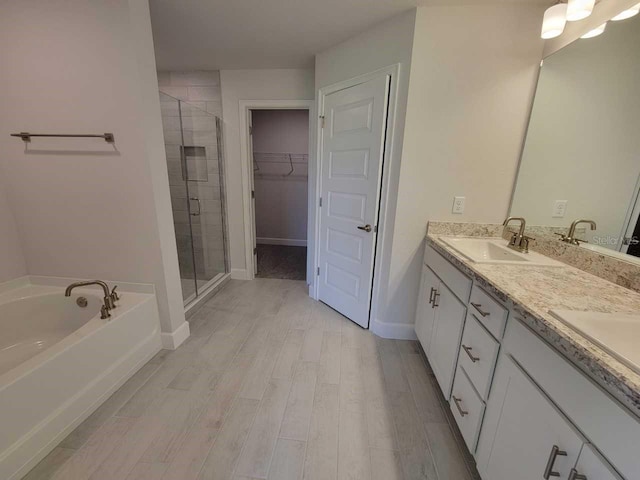 full bath with a garden tub, wood finished floors, a stall shower, a sink, and a walk in closet