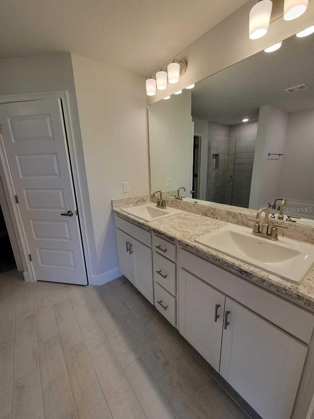 bathroom with a shower stall, double vanity, and baseboards
