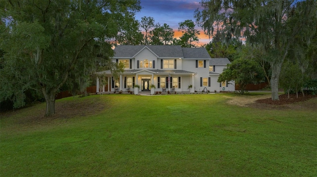 back house at dusk with a yard and covered porch