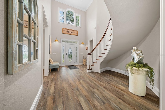 entrance foyer featuring dark wood-style flooring, a high ceiling, crown molding, baseboards, and stairs