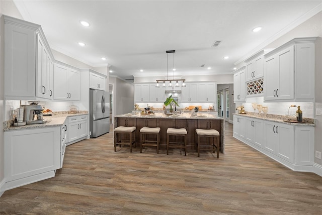 kitchen featuring visible vents, a breakfast bar, wood finished floors, a center island, and freestanding refrigerator