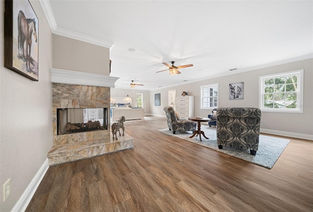 living area with a multi sided fireplace, a healthy amount of sunlight, wood finished floors, and ornamental molding