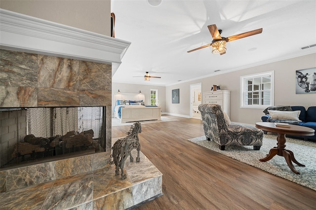 living area featuring wood finished floors, baseboards, visible vents, ornamental molding, and a tiled fireplace