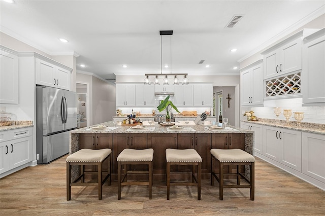 kitchen featuring visible vents, stainless steel fridge, a kitchen breakfast bar, and a kitchen island