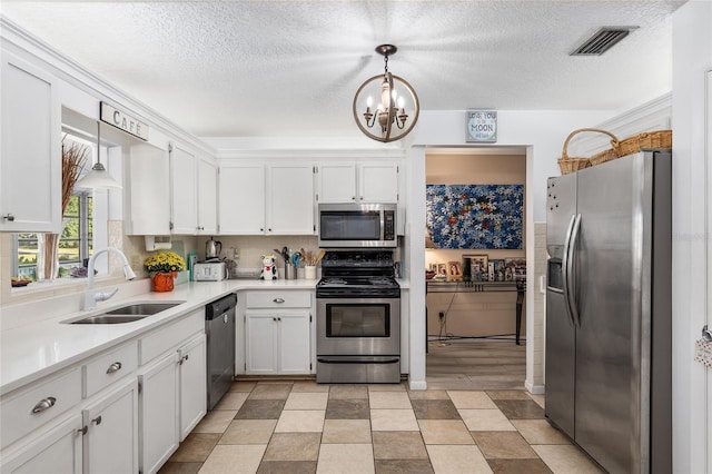 kitchen with appliances with stainless steel finishes, sink, pendant lighting, an inviting chandelier, and white cabinets