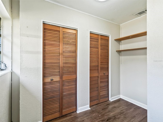 unfurnished bedroom with crown molding, dark hardwood / wood-style flooring, and two closets