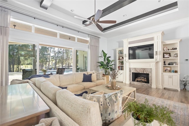 living room with ceiling fan, crown molding, beam ceiling, hardwood / wood-style flooring, and a premium fireplace