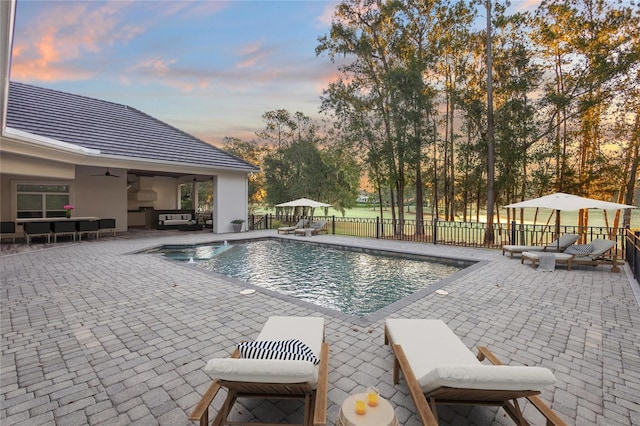 pool at dusk with ceiling fan, a patio area, and an outdoor hangout area