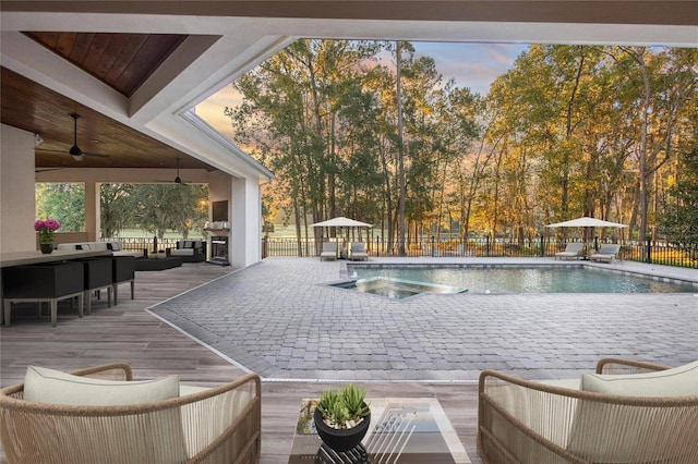 pool at dusk featuring ceiling fan and a bar