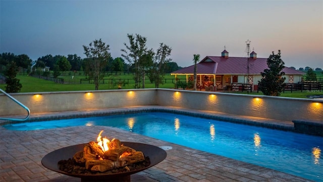 pool at dusk with a patio area and a fire pit