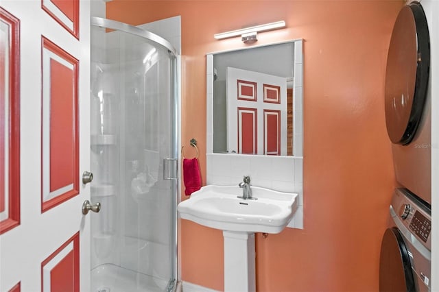 bathroom with backsplash, a shower with door, and stacked washer and clothes dryer