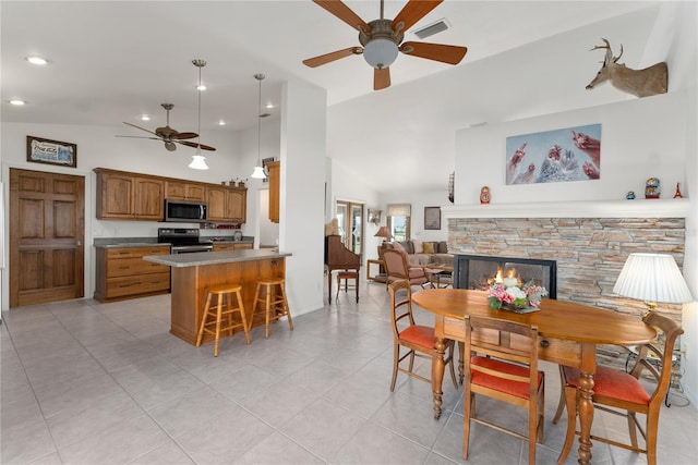 tiled dining space featuring a fireplace, ceiling fan, and lofted ceiling