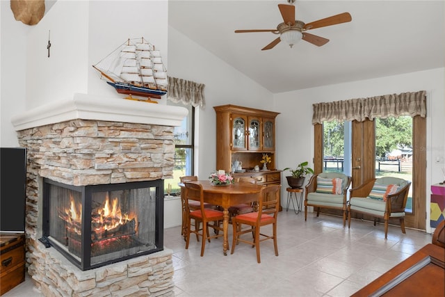 dining room with ceiling fan, a stone fireplace, lofted ceiling, and a wealth of natural light