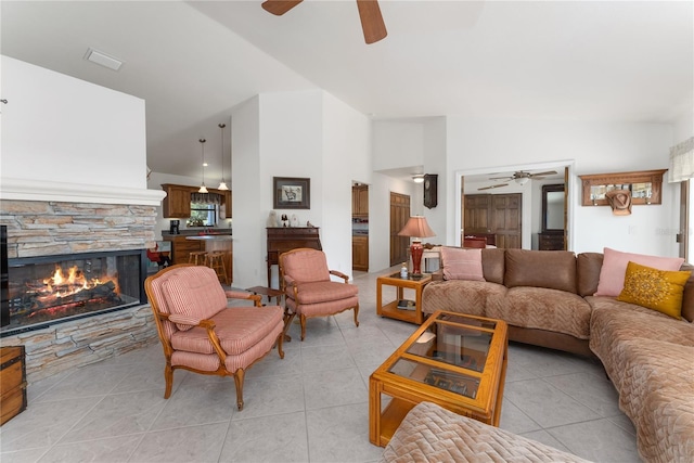 living room with a stone fireplace, ceiling fan, light tile patterned floors, and vaulted ceiling