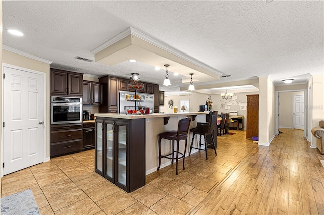 kitchen featuring a textured ceiling, stainless steel appliances, a kitchen island with sink, light hardwood / wood-style floors, and hanging light fixtures