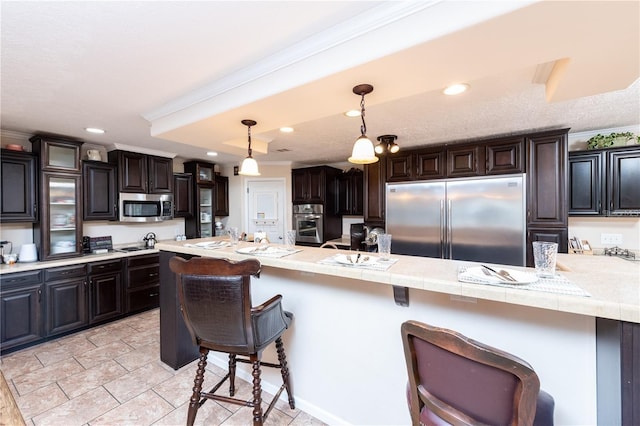 kitchen featuring a kitchen bar, appliances with stainless steel finishes, kitchen peninsula, dark brown cabinets, and decorative light fixtures