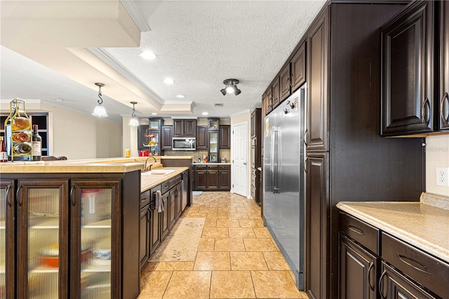 kitchen featuring stainless steel appliances, pendant lighting, a tray ceiling, dark brown cabinets, and ornamental molding