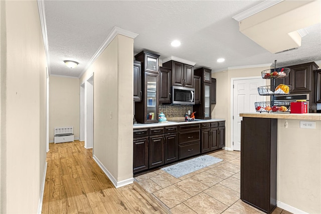 kitchen featuring light wood-type flooring, tasteful backsplash, ornamental molding, a textured ceiling, and dark brown cabinetry