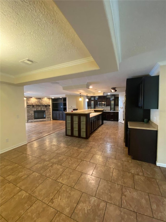 kitchen with a raised ceiling, a stone fireplace, a textured ceiling, a kitchen island, and ornamental molding