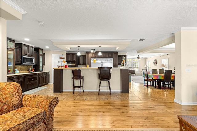 kitchen featuring appliances with stainless steel finishes, a textured ceiling, pendant lighting, a center island, and light hardwood / wood-style floors