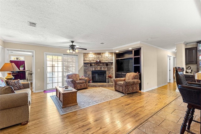 living room with ceiling fan, crown molding, light hardwood / wood-style floors, a textured ceiling, and a fireplace