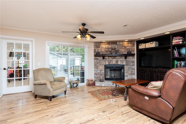 living room featuring a stone fireplace, crown molding, light hardwood / wood-style flooring, and a textured ceiling