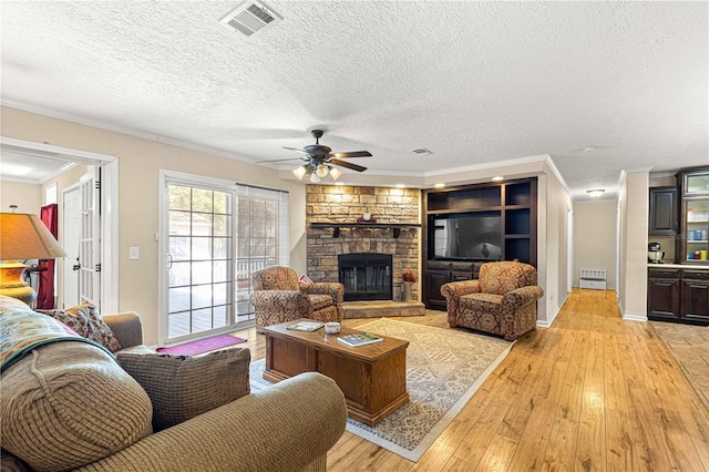 living room with a fireplace, light hardwood / wood-style flooring, a textured ceiling, and ornamental molding