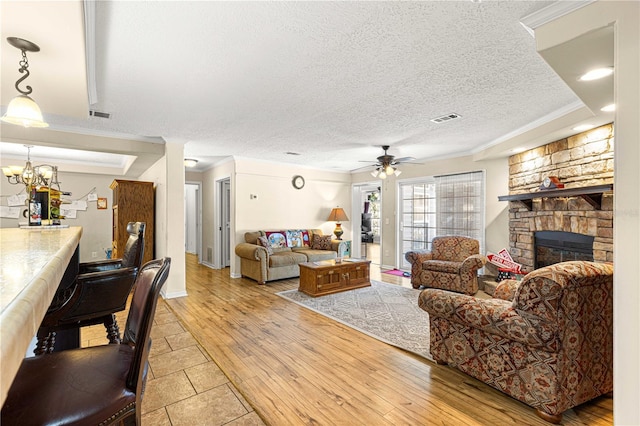 living room featuring ceiling fan with notable chandelier, ornamental molding, a fireplace, and light hardwood / wood-style flooring