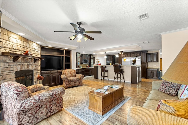 living room with a textured ceiling, light wood-type flooring, a stone fireplace, and ornamental molding