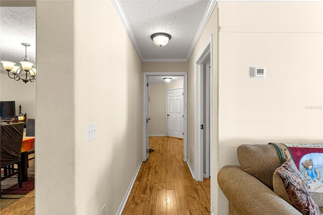 hall with a notable chandelier, light hardwood / wood-style floors, ornamental molding, and a textured ceiling