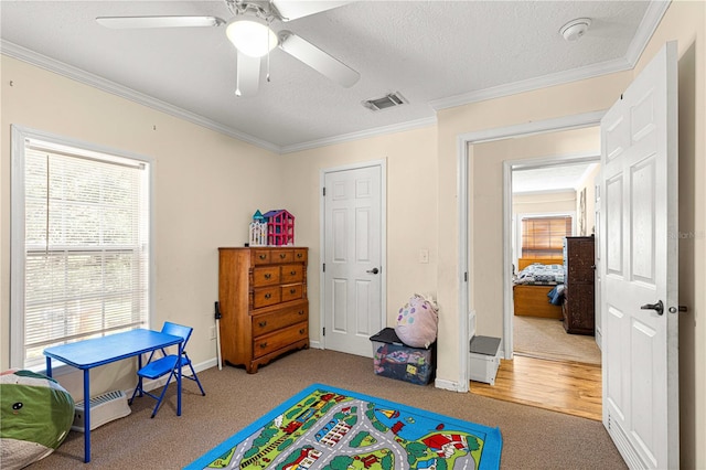 recreation room with light carpet, a textured ceiling, ceiling fan, and ornamental molding